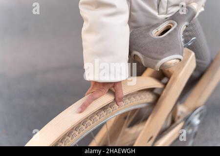 Von oben anonyme Frau in Oberbekleidung berühren Rad von Holz umweltfreundliche Fahrrad, während auf der Straße der Stadt stehen. Stockfoto