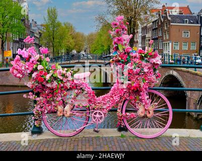 Altes Vintage-Fahrrad mit rosa Blumen auf einer kleinen Brücke im alten Teil von Amsterdam dekoriert Stockfoto