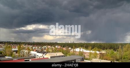 Regensturm über der Stadt, schwere Wolken fliegen über Häuser und Wald, Hurrikan kommt Stockfoto