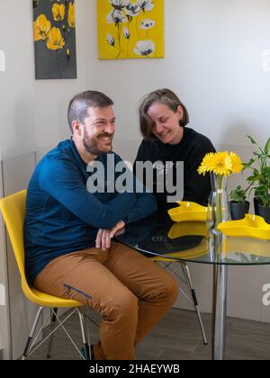 TOLEDO, SPANIEN - 29. Okt 2021: Ein glückliches hispanisches Paar sitzt an einem Tisch mit schönen Blumen in der Vase in der Küche Stockfoto