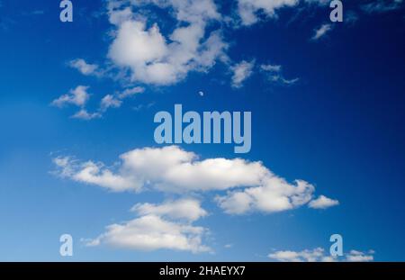 Weiße Wolken und der Mond am tiefblauen Sommerhimmel Stockfoto