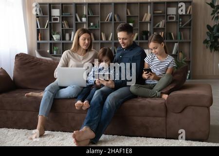 Glückliche Familie mit verschiedenen Gadgets zu Hause. Stockfoto