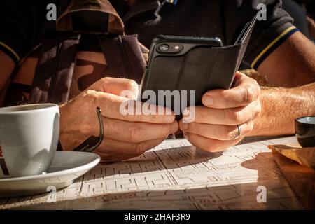 Mans Hände mit Mobiltelefon draußen sitzen an einem französischen Straßencafé Tisch Stockfoto