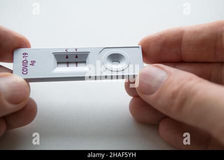 Rapid Antigen Detection Test (RADT) mit zwei roten Streifen, die ein POSITIVES Ergebnis eines Tests mit menschlichen Proben zeigen. Mans Finger halten den weißen Kunststoff d Stockfoto