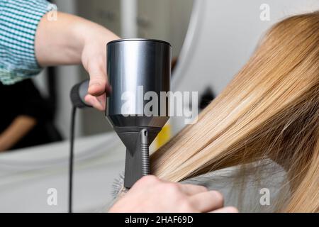 Close-up männlich professionellen Friseur Stylistin Hand halten Frau lange stark glatt glänzend gefärbt goldenen Haarverschluss und Trockner. Weibliche Person Kunde neu Stockfoto