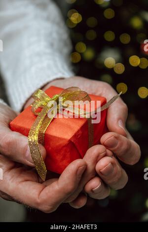 Weihnachts-Neujahrskarte.elegante rote Geschenkbox mit Goldband in den Händen des Mannes auf festlichen Weihnachtshintergrund.angenehme Feiertage Überraschungen und Geschenke Stockfoto