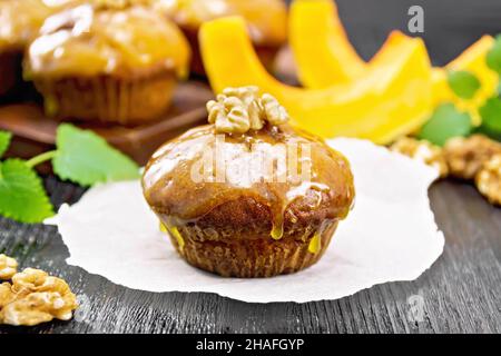 Kleiner Kürbis-Cupcake mit orangefarbener Glasur und Walnüssen auf Pergament, Minze-Zweige auf Holzbrett-Hintergrund Stockfoto