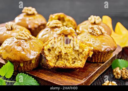 Kleine Kürbis-Cupcakes mit orangefarbener Glasur und Walnüssen, Minze-Zweige auf dunklem Holzbrett-Hintergrund Stockfoto