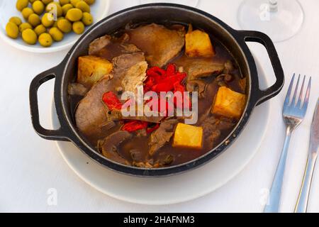 Traditionelle deutsche Geschmorte Schweinebäckchen in Braun Rotweinsauce mit Pilzen und Zwiebeln als closeup in einer Kasserolle Stockfoto