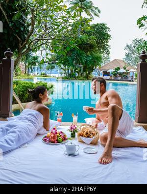 Das Paar frühstückte vor ihrem Zimmer am Pool in Thailand. Mann und Frau mittleren Alters im Urlaub beim Frühstück am Pool gerade mit Kaffee aufwachen Stockfoto