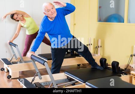 Älterer Mann, der Übungen der Heilgymnastik auf Pilates Reformer in der Reha-Klinik macht. Physikalische Medizin Konzept .. Stockfoto