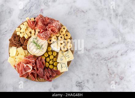 Blick von oben auf die leckere Wurstplatte mit Käse, Trauben, Nüssen, Oliven und Schinken auf einem runden Küchenteller Stockfoto