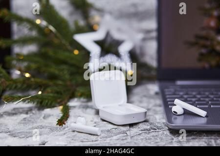 Kabellose Kopfhörer und Laptop in der Nähe von Weihnachtsdekorationen. Freiberuflich, Remote-Arbeit, Webinar-Teilnahme, Telefonieren mit Familie Konzept. Weihnachten, Neujahr vor Stockfoto