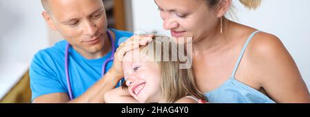Der Arzt untersucht das kranke Mädchen, das auf dem Schoß der Mutter sitzt Stockfoto