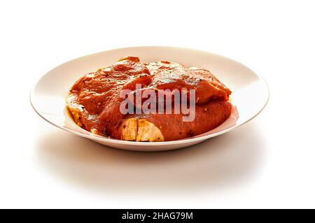 Schweinefleisch in Marinade liegt auf einem weißen Teller auf einem weißen isolierten Hintergrund Stockfoto