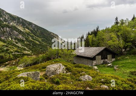 KARPACZ, POLEN - 09. Mai 2018: Eine Holzhütte auf dem grünen Gras neben einem Wald im Karkonosze-Gebirge. Stockfoto