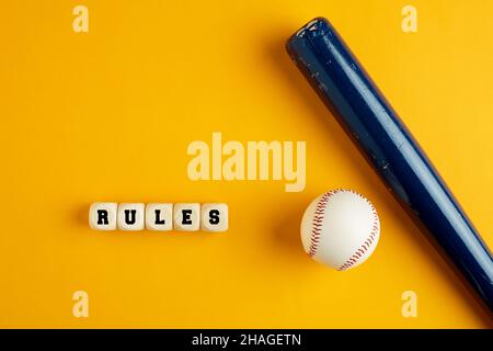 Hölzerner Baseballschläger und ein Ball auf gelbem Hintergrund mit dem Wort rules. Baseballregeln Konzept. Stockfoto