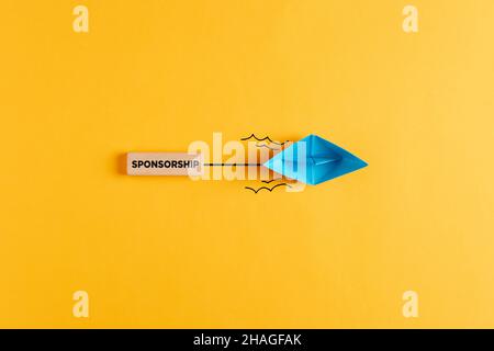 Papierboot zieht ein hölzernes Banner mit dem Wort Sponsoring. Sponsoring, finanzielle Unterstützung oder Fundraising-Konzept. Stockfoto