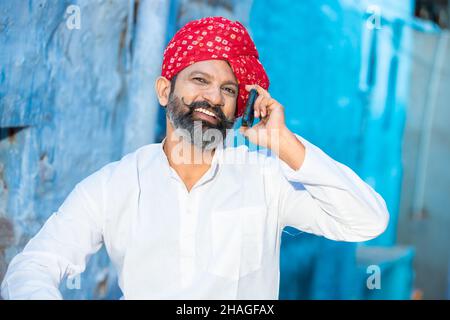 Happy North Indian reifen Mann mit Bart und roten Turban im Gespräch auf Smartphone, lächeln traditionellen männlichen Anruf auf android-Smartphone, während s Stockfoto