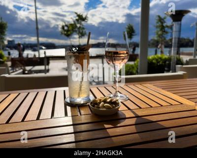 Zwei Gläser Wein und Cocktails mit Himmel und Sonne auf einem Tisch in einem Restaurant am Wasser, Sydney Stockfoto