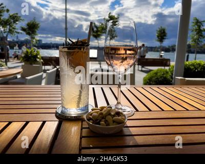 Zwei Gläser Wein und Cocktails mit Himmel und Sonne auf einem Tisch in einem Restaurant am Wasser, Sydney Stockfoto