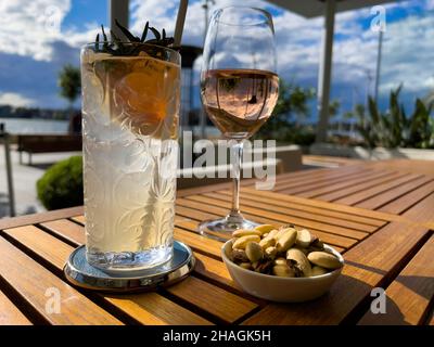 Zwei Gläser Wein und Cocktails mit Himmel und Sonne auf einem Tisch in einem Restaurant am Wasser, Sydney Stockfoto