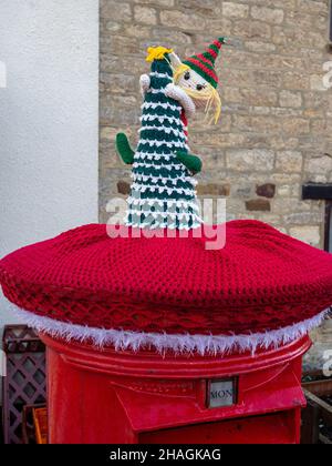 Red Royal Mail Briefkasten mit einer gestrickten Weihnachtsdekoration oder Garn Bombing gekrönt, in dem Dorf Hackleton, Northamptonshire, Großbritannien Stockfoto