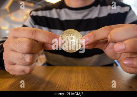 Die Hand des Mannes hält eine goldene Bitcoin-Münze. Foto des Investitionskonzepts für Kryptowährungen. Stockfoto