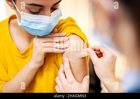 Globale Impfungen und Gesundheitsfürsorge. Die Nahaufnahme der Krankenschwester, die nach der Injektion einen klebrigen Verbandsputz auf den Arm des Mädchens legte, kovid 19-Impfstoff. Stockfoto