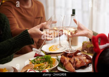 Partygäste klirren Gläser mit Weißwein über den weihnachtlichen Esstisch Stockfoto