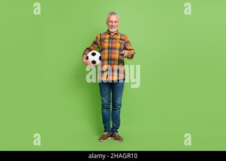 In voller Größe Foto von niedlichen Elder Bart Mann Uhr Fußball tragen Hemd Jeans Schuhe isoliert auf grünem Hintergrund Stockfoto