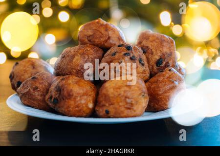 „Oliebollen“, traditionelles holländisches Gebäck für Silvester mit Glitzern. Ölknödel oder Fritter mit Zuckerpulver darauf. Weihnachtsbaum Lichter Bokeh auf dem Hintergrund. Typisches Essen. Selektiver Fokus Stockfoto