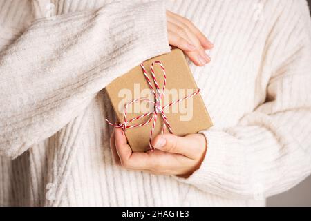 Frau in gemütlichen beige gestrickten Pullover geben weihnachten Handwerk Geschenkboxen mit rotem Band. Geben Geschenke Konzept.Valentinstag und Muttertag Geschenk-Konzept. Stockfoto