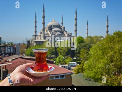 Hand der Frau hält Tasse mit traditionellem türkischen Tee vor der Blauen Moschee alias Sultanahmet Camii in Istanbul, Türkei. Istanbuls Hauptattraktionen. Stockfoto