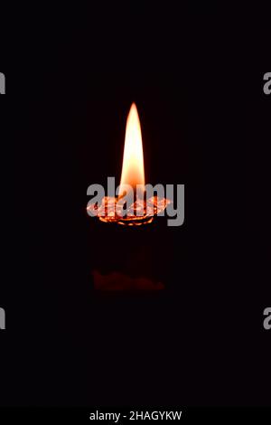 Eine einsame, geschmolzene Kerze brennt im Dunkeln. Auf einem dunklen Hintergrund. Nahaufnahme. Stockfoto