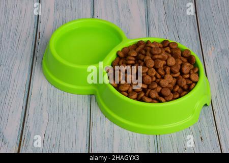 Vor dem Hintergrund von Holzbrettern liegt eine grüne Kunststoffplatte gefüllt mit Trockenfutter zur Fütterung von Katzen oder Hunden und Wasser. Stockfoto
