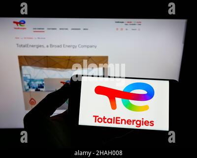 Person mit Mobiltelefon und Logo des französischen Öl- und Gasunternehmens TotalEnergies SE auf dem Bildschirm vor der Webseite. Konzentrieren Sie sich auf die Telefonanzeige. Stockfoto