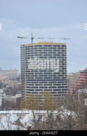 Ein unvollendeter Wolkenkratzer, hinter dem ein Hochhaus-Turmkran in einer Winterstadt steht. Aus der Ferne aufgenommen Stockfoto