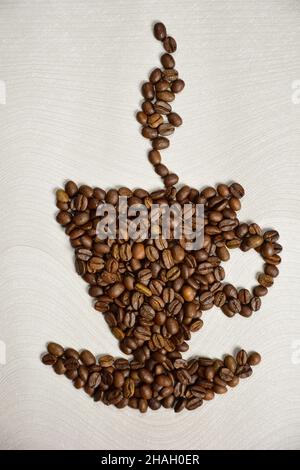 Aus Kaffeebohnen wird eine Figur in Form einer Tasse Kaffee mit einer Untertasse und Dampf darüber gelegt Stockfoto