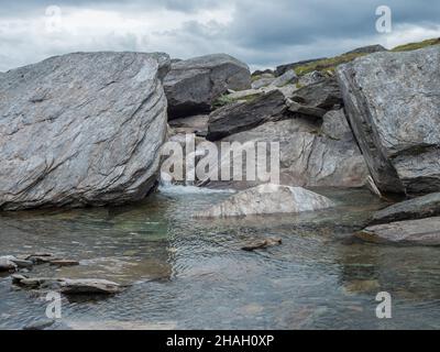 Das Wasser fließt über die Spitze der großen grauen Steinbrocken am Wasserstrom in der arktischen nördlichen Landschaft in Schwedisch Lappland Stockfoto