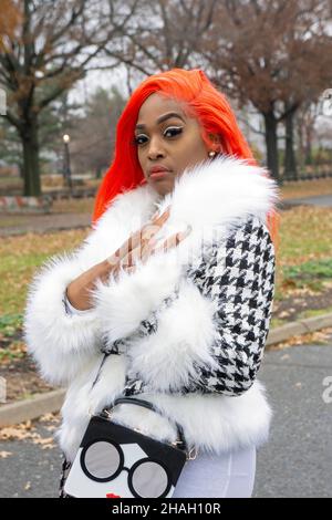 Posierte Porträt einer hübschen Dame mit orangefarbenen Haaren und langen Fingernägeln. In einem Park in Queens, New York City. Stockfoto