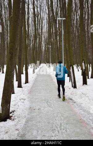 Ein Einzelkämpfer, der in einer Sportuniform auf einer schneebedeckten Strecke in einem Winterpark joggt Stockfoto