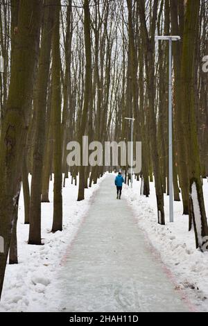 Ein Einzelkämpfer, der in einer Sportuniform auf einer schneebedeckten Strecke in einem Winterpark joggt Stockfoto