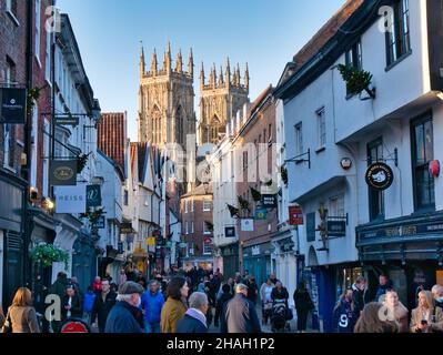 Die überfüllte Einkaufsstraße von Low Petergate an einem sonnigen Tag in York, Yorkshire, Großbritannien im November 2021. Dahinter erscheinen die Zwillingstürme des York Minster. Stockfoto