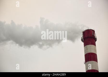 Dampfender, gestreifter Kamin einer Pflanze oder Fabrik auf einem Himmelshintergrund Stockfoto