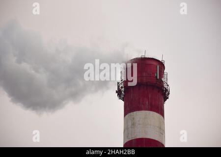 Dampfender, gestreifter Kamin einer Pflanze oder Fabrik auf einem Himmelshintergrund Stockfoto