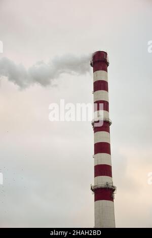 Dampfender, gestreifter Kamin einer Pflanze oder Fabrik auf einem Himmelshintergrund Stockfoto