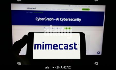 Person, die das Smartphone mit dem Logo des E-Mail-Management-Unternehmens Mimecast Services Limited auf dem Bildschirm vor der Website hält. Konzentrieren Sie sich auf die Telefonanzeige. Stockfoto