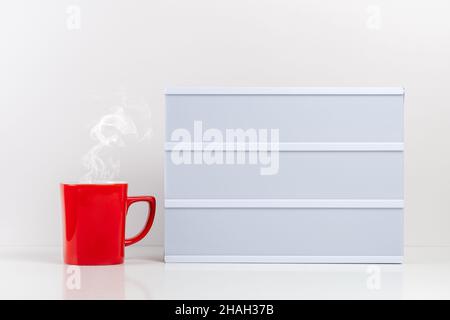 Rote Tasse Kaffee mit leerem Text-Leuchtkasten auf weißem Tisch. Modell-Konzept. Stockfoto