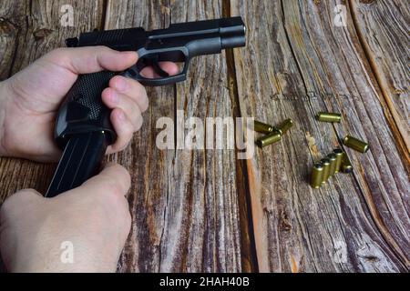 Traumatische Patronen sind auf einem braunen Holzhintergrund verstreut. Hände halten einen Pistolenclip und eine Pistole Stockfoto